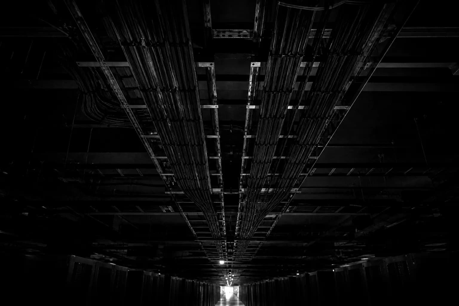 Overhead cable trays carrying bundled fibre trunks along a dark data centre hall